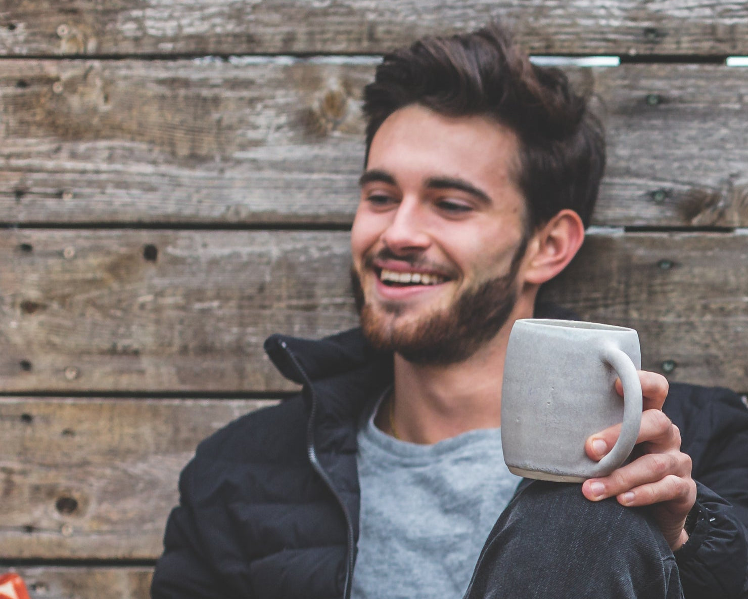 Man sitting outdoors holding a mug, smiling