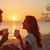 Couple enjoying coffee on a beach at sunset with 'buen dia coffee co.' logo.