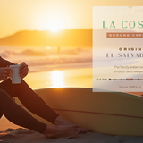 Man in a wetsuit sitting on a surfboard at sunset with a coffee cup, La Costa coffee label overlay.