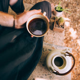 Person holding a cup of coffee outdoors with plants in the background
