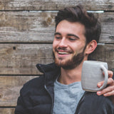 Man sitting outdoors holding a mug, smiling