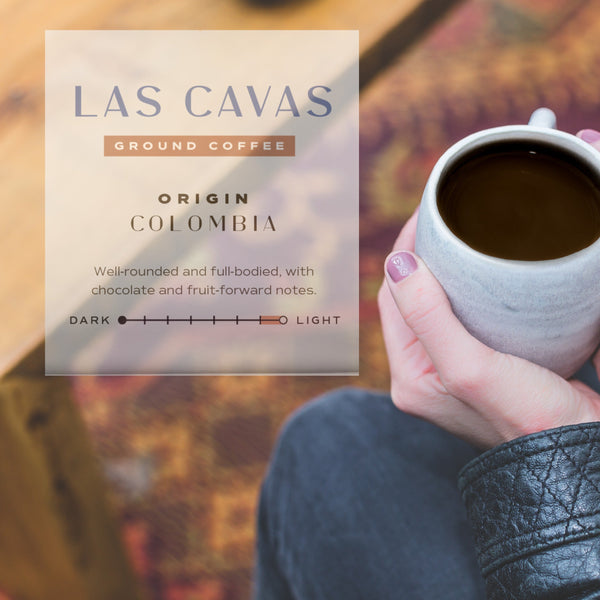 Person holding a mug of coffee with Las Cavas coffee packaging in the foreground